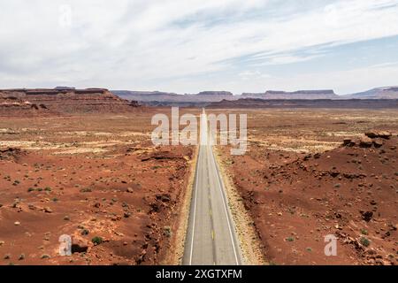 Un'immagine accattivante che mostra una strada rettilinea che attraversa lo splendido paesaggio desertico della Valle degli dei, Utah, sotto un vasto cielo nuvoloso Foto Stock