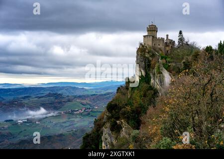 Un'immagine suggestiva che cattura la prima Torre Guaita del Castello di San Marino, arroccata sulla cima di aspre scogliere, con una vista panoramica delle colline verdeggianti a Foto Stock
