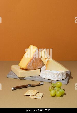 Dall'alto, una varietà di formaggi tra cui Brie, Swiss e Cheddar, abbinati elegantemente a cracker e uva, posizionati su una superficie beige testurizzata Foto Stock