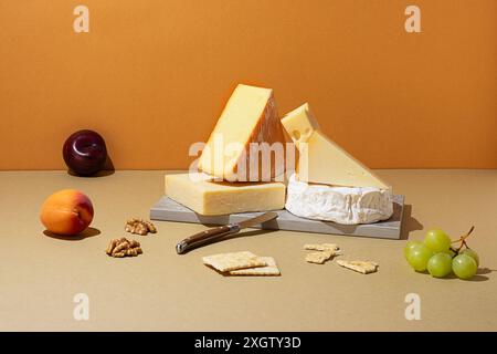 Vista dall'alto dei formaggi assortiti insieme a frutta e noci su una superficie dai colori neutri. La composizione comprende brie, cheddar e swiss, completata da Foto Stock