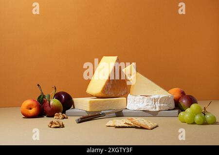 Vari formaggi accompagnati da frutta fresca tra cui mele, uva e albicocche assemblate elegantemente su una superficie beige Foto Stock
