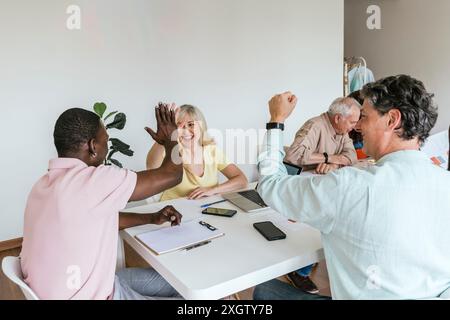 Gruppo multietnico di colleghi impegnati in un incontro collaborativo in uno spazio di coworking, celebrando un progetto di successo che condivide un momento gioioso indi Foto Stock