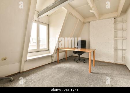 Un luminoso e semplice ufficio attico con una scrivania in legno, sedia nera e scaffalature incassate, situato in Joan Melchior Kemperstraat, Amsterdam, Paesi Bassi Foto Stock
