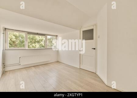 Camera spaziosa e luminosa con grande finestra con vista verde, pavimenti in legno e porta bianca. Foto Stock