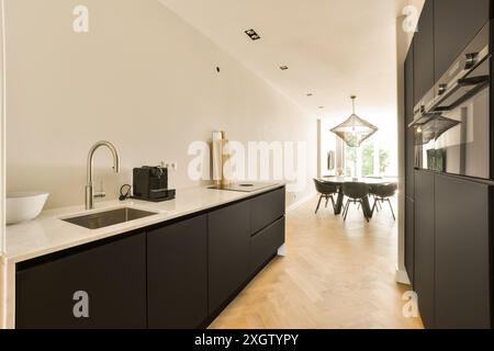 Una cucina spaziosa e ben illuminata con armadi neri e una zona pranzo con una lampada a sospensione unica. Foto Stock
