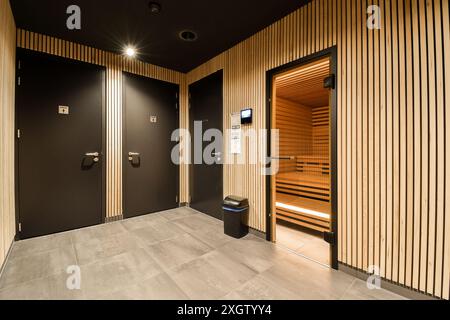 Moderno bagno del centro fitness caratterizzato da eleganti lastre di legno, porte scure a contrasto e una sauna invitante, che trasuda un senso di lusso e relax Foto Stock