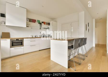 Uno spazio cucina contemporaneo con mobili bianchi, elettrodomestici in acciaio inox e un bar in legno con sgabelli grigi. Foto Stock