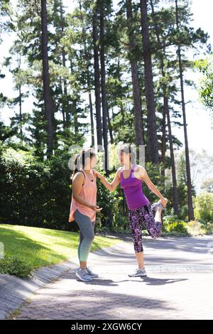 Amiche asiatiche felici che indossano abiti sportivi e si allungano nel parco. Fitness, esercizio fisico, attività, amicizia e stile di vita, inalterati. Foto Stock