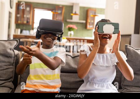 Fratello e sorella birazziali adolescenti si divertono con i giochi VR a casa. Le loro risate riempiono la stanza mentre esplorano mondi virtuali insieme. Foto Stock