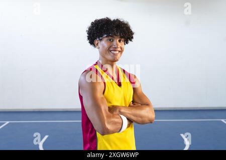 Il giovane uomo birazziale si posa con sicurezza su un campo da basket, incarnando uno stile di vita sportivo. La sua uniforme da basket suggerisce che è pronto per una partita o un pr Foto Stock
