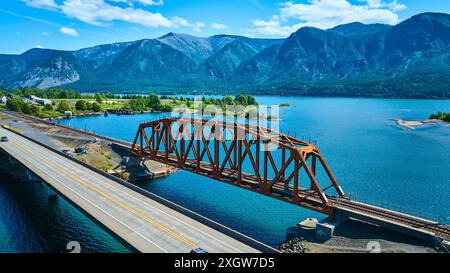 Volo aereo attraverso il Red Metal Bridge sul tranquillo lago con sfondo montano Foto Stock