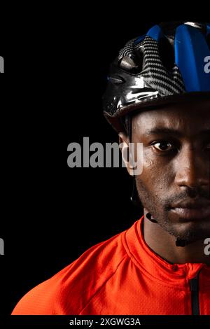 Ciclista afro-americano che indossa un casco, con spazio per le copie su sfondo nero. Il suo sguardo intenso suggerisce determinazione e prontezza per la co Foto Stock