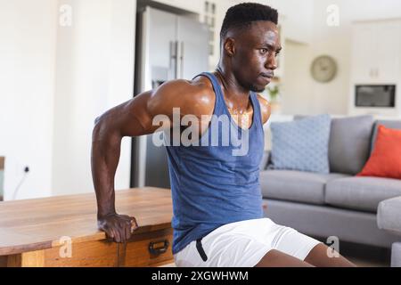 Adatta un uomo afroamericano che lavora a casa, facendo push up usando il tavolino da caffè. Fitness, allenamento, esercizio, vita domestica e stile di vita sano, una Foto Stock