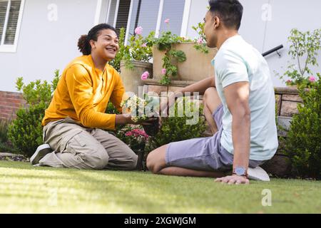 Uomo birazziale e uomo mediorientale che giardinano insieme all'aperto. Condividono un momento di gioia durante un'attività di giardinaggio a casa. Foto Stock