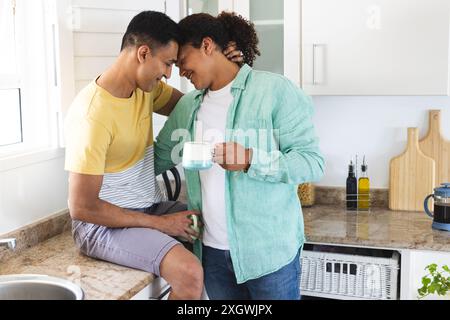 La coppia gay birazziale gode di un momento accogliente in cucina. Condividono una connessione calda con un caffè mattutino a casa. Foto Stock