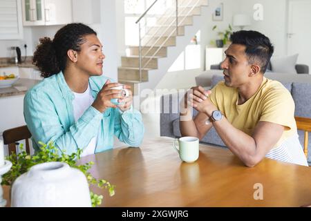 Il giovane uomo birazziale e il mediorientale, una coppia gay, condividono una conversazione con un caffè a casa. Si godono una mattinata rilassata in un luminoso e moderno ki Foto Stock