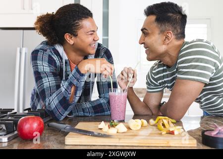 Diverse coppie gay si godono un frullato a casa. Condividono un momento divertente in un ambiente accogliente in cucina. Foto Stock