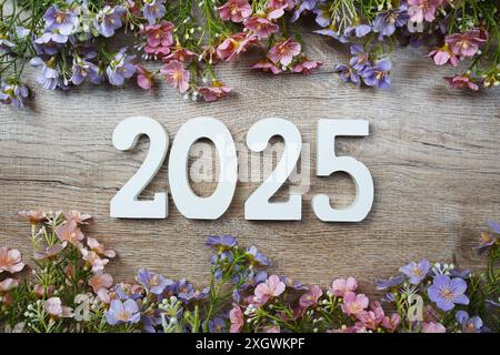 numero di anni 2025 con vista dall'alto della cornice dei fiori su sfondo in legno. Buongiorno, benvenuto e addio al nuovo anno Foto Stock