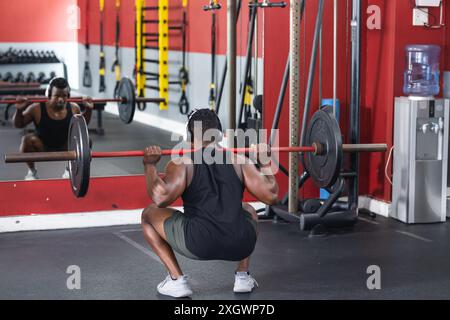 Un uomo afroamericano in forma esegue uno squat in palestra. La sua attenzione al fitness è evidente nello spazio ben attrezzato per gli allenamenti. Foto Stock