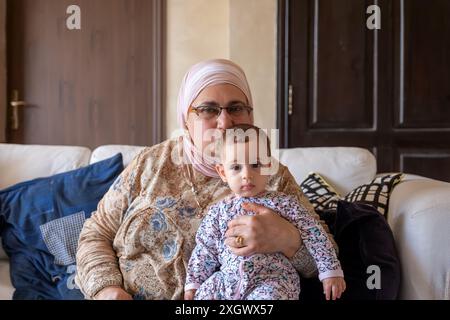 Nell'accogliente soggiorno, una nonna tiene con gioia sua nipote, che irradia emozioni e amore in questo bellissimo momento della loro vita Foto Stock