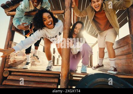 Amici felici che posano, sorridono e ridono in un parco giochi in legno all'aperto. Momento vivace e gioioso con gente allegra che si diverte. Foto Stock