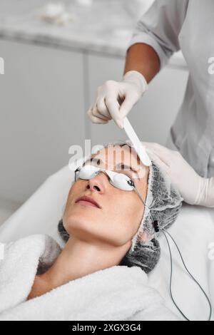 Una donna applica il gel al viso prima di una procedura laser. Foto Stock