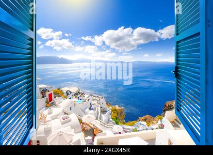Vista sulle colline attraverso una finestra aperta con persiane blu della caldera, del mare e del villaggio bianco di Oia sull'isola di Santorini, in Grecia. Foto Stock