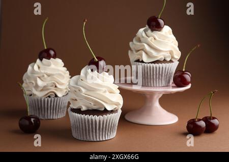 Deliziosi cupcake con panna e ciliegie su sfondo marrone Foto Stock