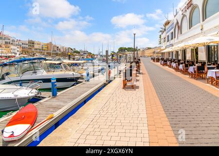 Le barche costeggiano il porto turistico presso il villaggio di pescatori di Ciutadella de Menorca, in Spagna, con negozi e caffetterie lungo la passeggiata costiera sull'isola di Minorca. Foto Stock