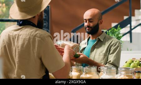 Commerciante che mostra condimenti e prodotti alimentari in contenitori o barattoli al cliente vegano mentre sta acquistando generi alimentari. Il consumatore medio-orientale vuole acquistare prodotti biologici e naturali. Foto Stock