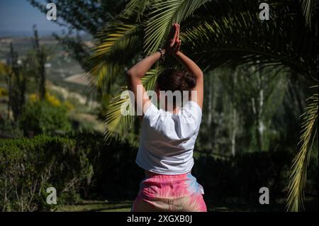 Una giovane donna si impegna in una posa yoga in un tranquillo ambiente all'aperto circondato da una vegetazione lussureggiante, promuovendo il relax e la consapevolezza. Foto Stock