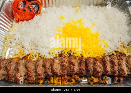 Piatto da asporto di cibo persiano: Riso basmati cosparso di riso allo zafferano, kabob koobideh, pomodoro intero grigliato Foto Stock