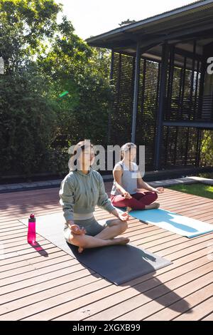 Due donne asiatiche praticano yoga all'aperto in una giornata di sole, con spazio fotocopie. Impegnati in una sessione di meditazione pacifica, contribuiscono a un sereno An Foto Stock