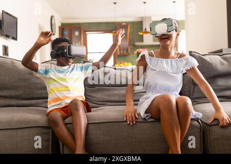 Fratello e sorella birazziali adolescenti si divertono con i giochi VR a casa. Sono immersi in un'esperienza di realtà virtuale, condividendo un momento di gioia ed eccitazione. Foto Stock