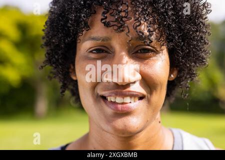 Primo piano di una giovane donna birazziale sorridente all'aperto, inalterata. La sua espressione allegra illumina l'ambiente soleggiato del parco. Foto Stock