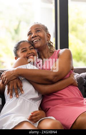 La nonna afroamericana senior abbraccia una nipote birazziale adolescente a casa. Il loro caldo abbraccio riflette uno stretto legame familiare e intergenerazione Foto Stock