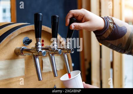 La persona da vicino versa il VIN brulé del rubinetto nella tazza di carta al mercato all'aperto gustando una bevanda calda il giorno d'inverno. Vend. Gluhwein self-service Foto Stock