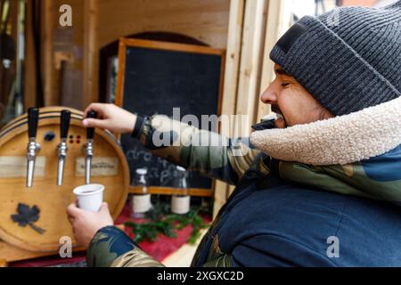 La persona versa del VIN brulé dalla spina nella tazza di carta al mercato all'aperto gustando una bevanda calda il giorno d'inverno. Fornitore self-service di gluhwein presso Christma Foto Stock