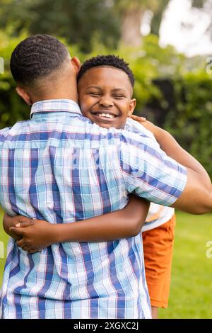 Il giovane padre afroamericano abbraccia un figlio afroamericano all'aperto. Il loro caldo abbraccio trasmette un senso di amore e sostegno familiare in un ambiente naturale Foto Stock