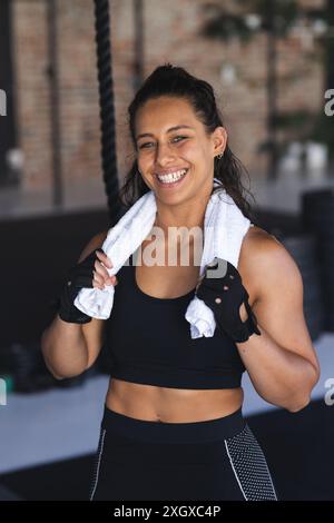 Una giovane donna birazziale in forma sorride dopo l'allenamento in palestra. Il suo abbigliamento sportivo e la sua brillante espressione mostrano il suo senso di soddisfazione e benessere, inalterato Foto Stock