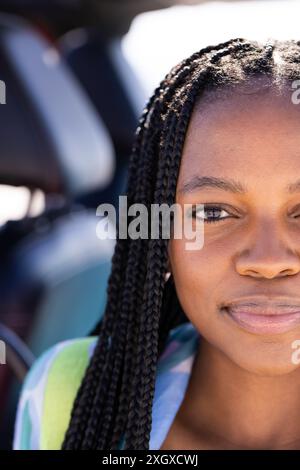Primo piano di una giovane donna afroamericana all'aperto durante un viaggio in auto. Il suo sguardo e il suo sorriso suggeriscono fiducia e positività in un ambiente soleggiato. Foto Stock
