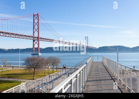 Passerella pedonale che attraversa la ferrovia per raggiungere la riva del Tago Reiver con il ponte iconico (Ponte 25 de Abril), sullo sfondo - Lisbona, Portogallo Foto Stock