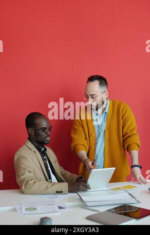 Due diversi colleghi maschi discutono i dettagli del progetto su un tablet digitale mentre collaborano in un ufficio moderno Foto Stock