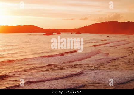 Un tramonto sereno su un oceano calmo con onde dolci e colline lontane. Foto Stock