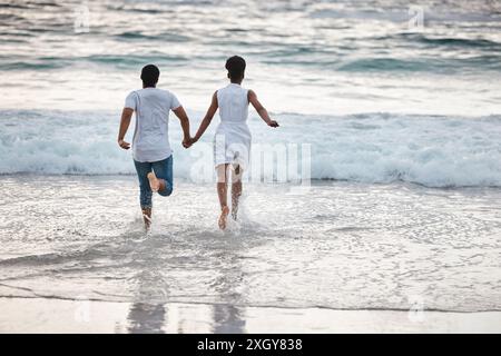 Corsa, coppia nera e acqua in vacanza, tenersi per mano o festeggiare l'anniversario. Vista posteriore, Splash e le persone viaggiano per il matrimonio Foto Stock