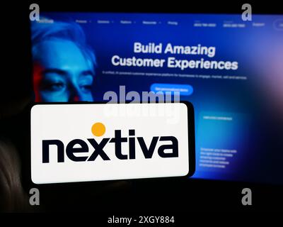 Persona che detiene un telefono cellulare con il logo della società americana di software per la comunicazione Nextiva Inc. Davanti alla pagina web. Mettere a fuoco il display del telefono. Foto Stock