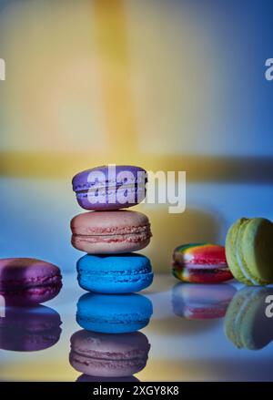 Un assortimento di macaron luminosi di diversi colori viene visualizzato su una superficie in vetro con uno sfondo decorativo astratto illuminato in pa diversi Foto Stock