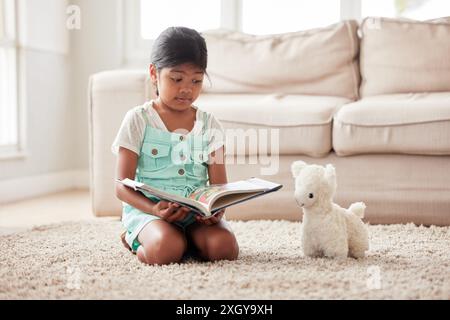 Giocattolo, gioco e ragazza che leggono libri a casa per imparare, legare e conoscere insieme in famiglia. Educazione, orsacchiotto e bambino su tappeto Foto Stock