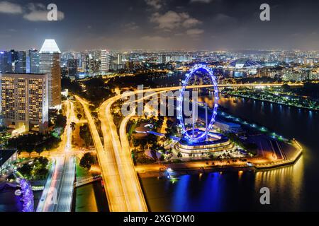 Splendida vista notturna del centro di Singapore. Vista dall'alto di Bayfront Avenue e della gigantesca ruota panoramica presso Marina Bay. Bellissimo paesaggio urbano. Foto Stock