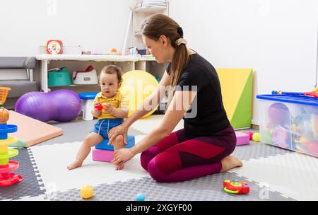 Fisioterapista che assiste un bambino con disturbi di coordinazione durante l'esercizio di sviluppo delle capacità motorie nella moderna clinica di riabilitazione. Fisioterapia Foto Stock